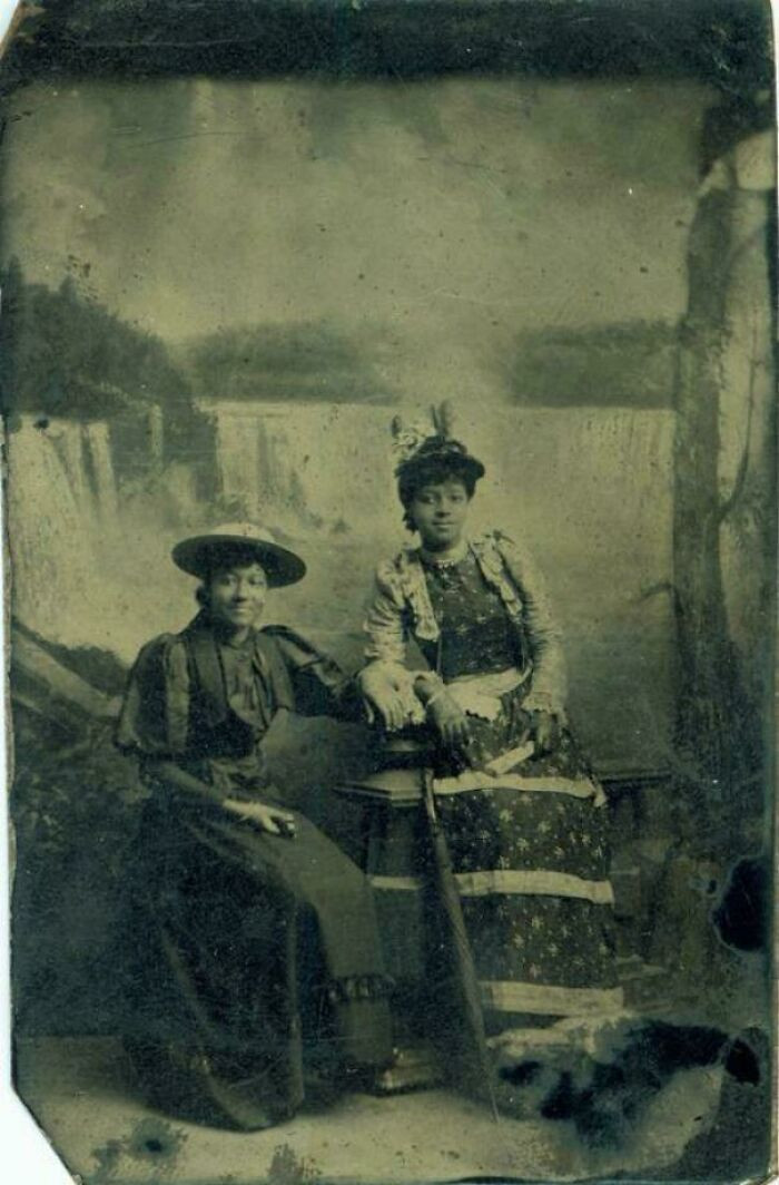 "A Formal Portrait Of Two Young Black Women Standing In Front Of A Faux Backdrop Featuring Niagara Falls, 1890s"