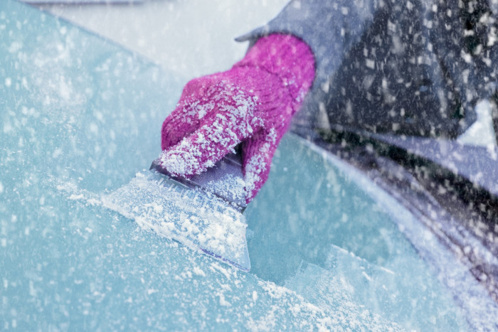 Driver applying quick DIY de-icer spray to clear a frosted windshield