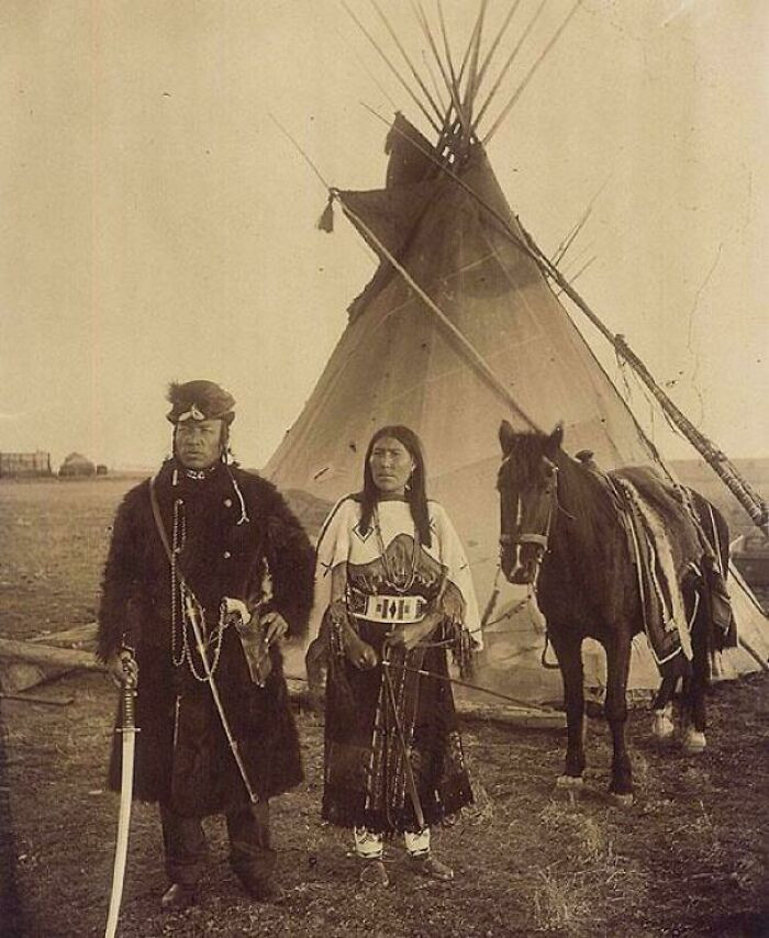 "Dog Child, A North West Mounted Police Scout, And His Wife, The Only Handsome Woman, Members Of The Blackfoot Nation, Gleichen, Alberta, 1890. Interesting That He Is Holding Japanese Sword"