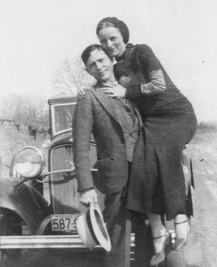 "Bonnie Parker And Clyde Barrow Smiling Beside A Ford V-8 In 1933; One Year Later, An Ambush Ended One Of The Most Extensive Manhunts America Had Yet Seen"