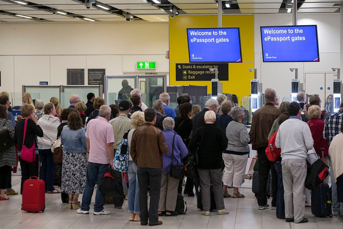 Airport departure hall sign warning of long waits during biometric border checks.