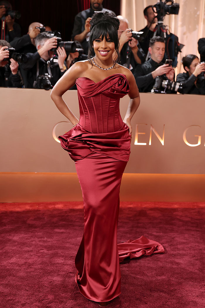 Mona Kosar Abdi dazzled in a deep red strapless gown with a sculpted corset and rose-like draping, finished with a diamond choker and a sleek updo with soft bangs.