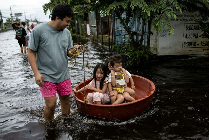 Children Sitting In A Basin React As They Are Pulled Through A Flooded Area On Manila North Road
