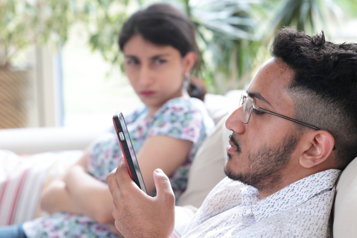 Person holds a phone while partner’s attention shifts, suggesting hidden unfaithfulness.