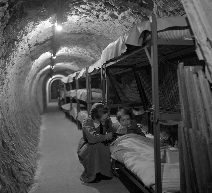 "Woman Kneeling Next To Bed Of Child, In An Underground Tunnel During The Bombing Of London, World War II, January 1945"