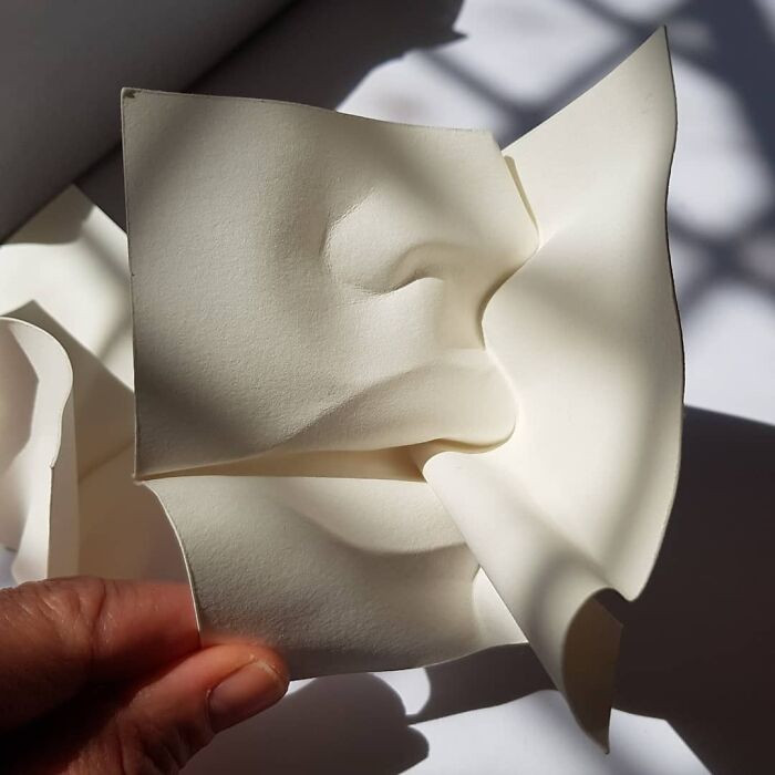 Paper portrait seen through layered folds, translucent veil effect with curved zigzag geometry.