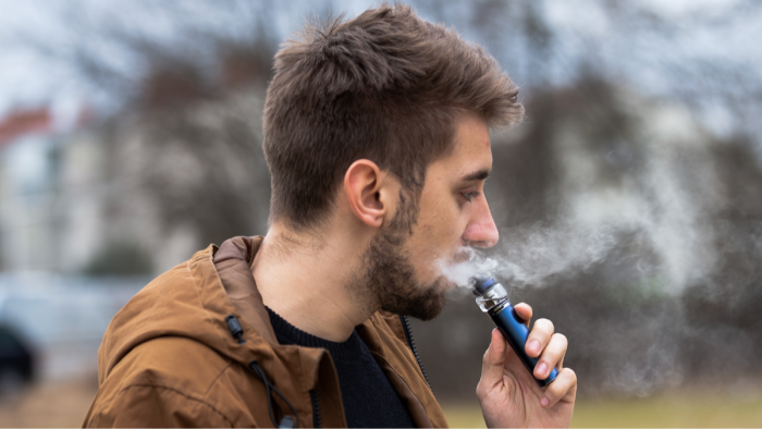 Close view of vape device near mouth, suggesting vaping impacts on gums and saliva