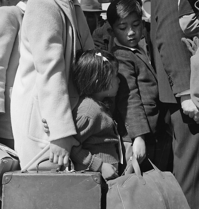 Third-generation American children of Japanese ancestry stand among the crowd as they wait for the next bus that will take them from their homes to the assembly center in Byron, California, in 1942.