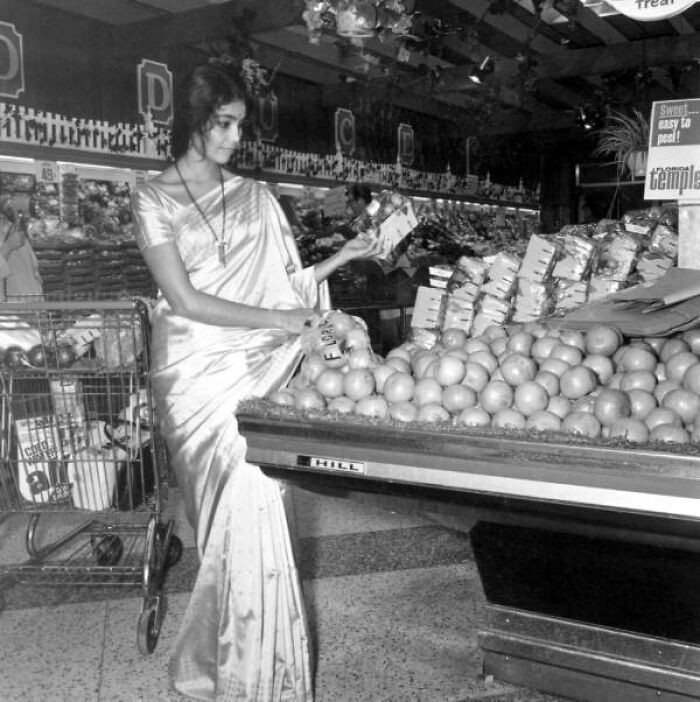"Woman Dressed In A Sari Examines Fruit In The Grocery Store, Tallahassee, Florida, 1971"