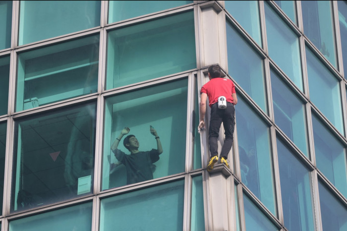Alex Honnold methodically climbs a tall skyscraper face, no safety ropes.