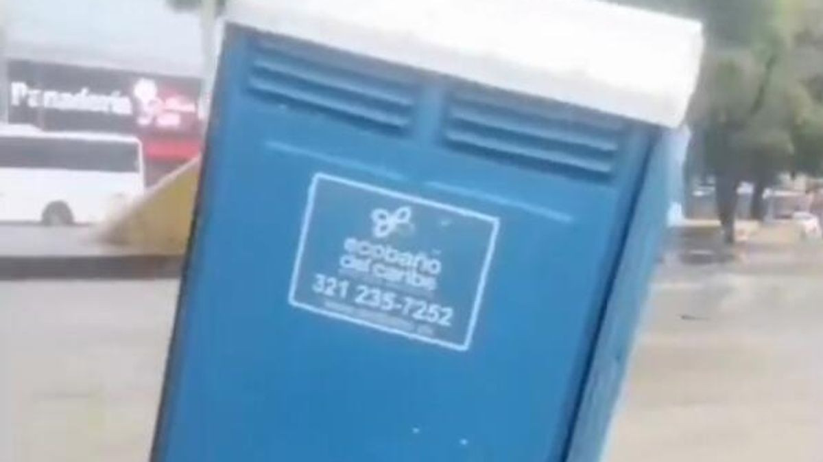 Man inside portable toilet is swept down flooded street before stranger drags it to safety