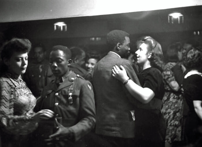 American soldiers unwind on a London pub dance floor during the 1940s, sharing laughs and music far from the front lines.