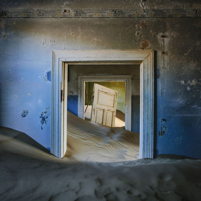10. A crooked wave of sand pushes past a half-broken door still trying to stand guard