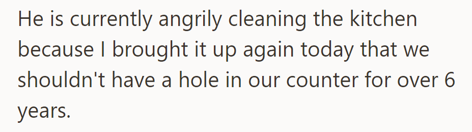 He's angrily cleaning the kitchen due to her reminder about the 6-year-old counter hole.